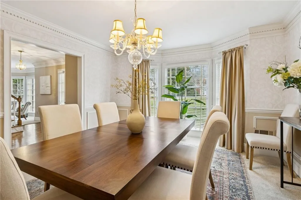 Dining room with hanging lights, wallpapered walls, a decorative wall, crown molding, and wainscoting