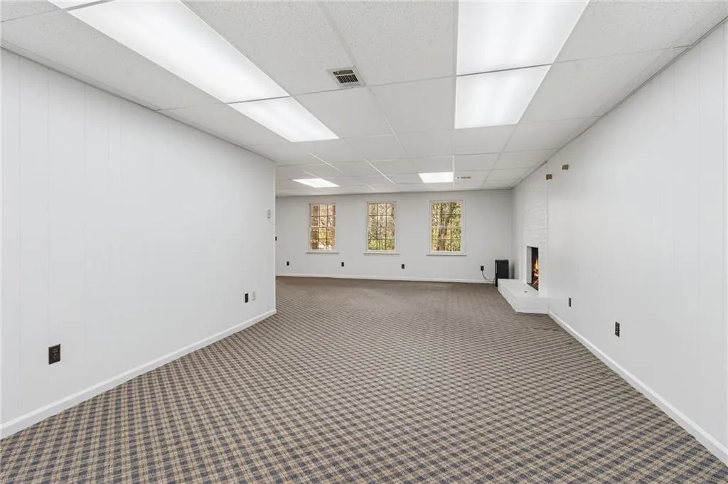 Empty room with wood walls, a drop ceiling, a brick fireplace, and carpet floors