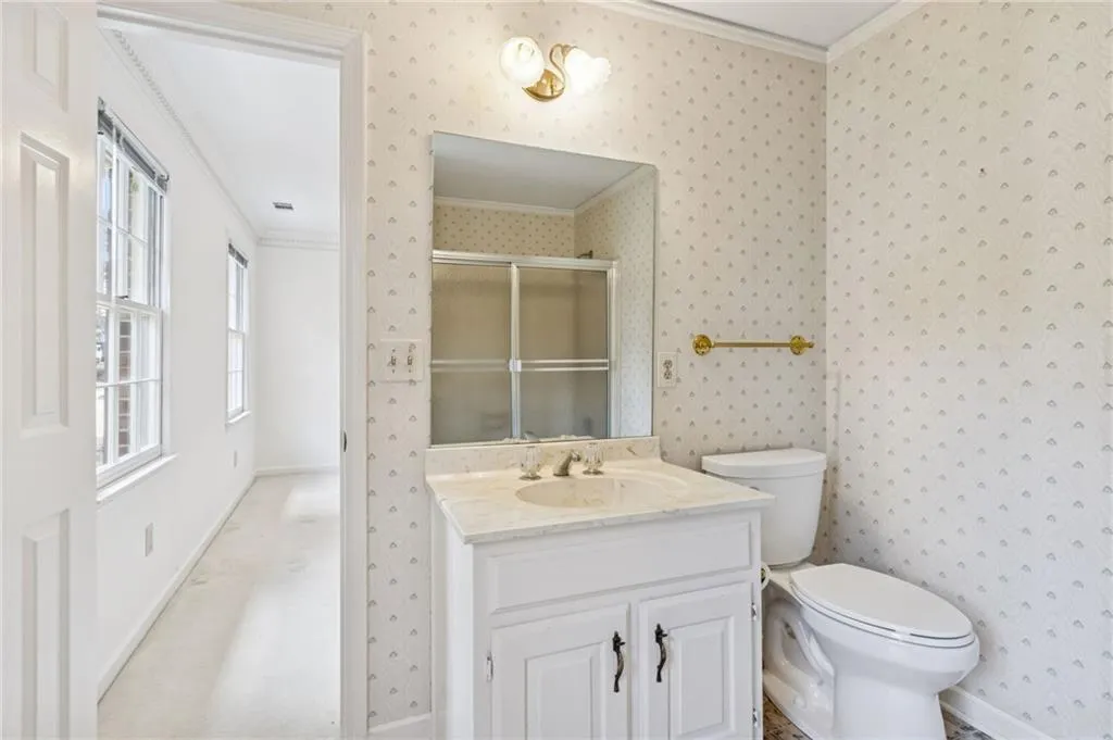 Bathroom with ornamental molding, wallpapered walls, a shower stall, and vanity