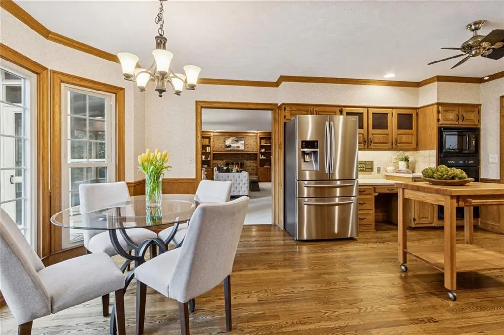 Dining room featuring ceiling fan, wood finished floors, suspended lighting, crown molding, and wainscoting