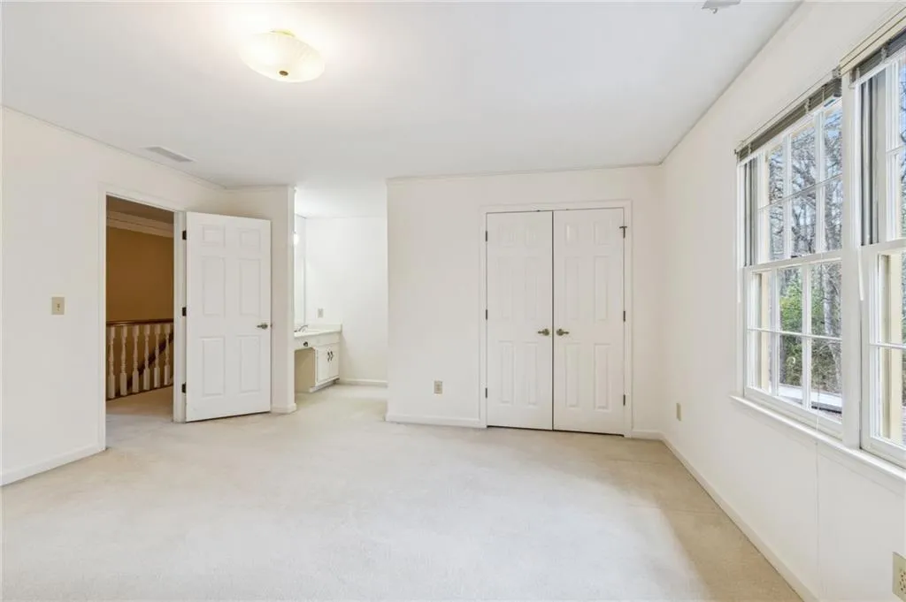 Unfurnished bedroom featuring ensuite bathroom, light carpet, and a closet