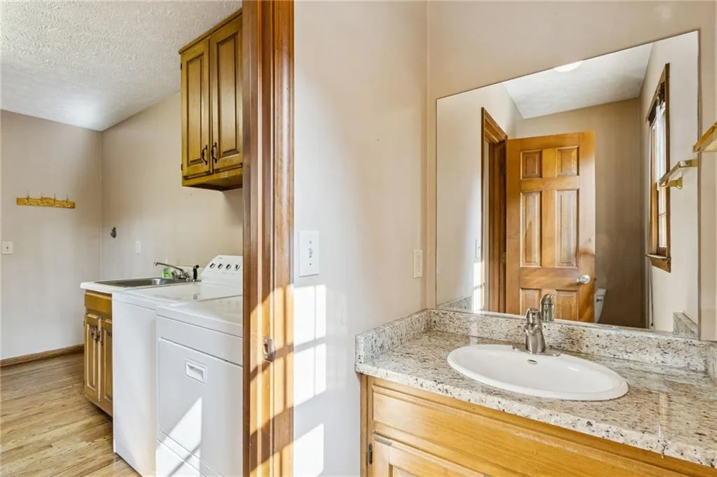 Half Bathroom with vanities in mudroom, light wood finished floors, a textured ceiling, and independent washer and dryer