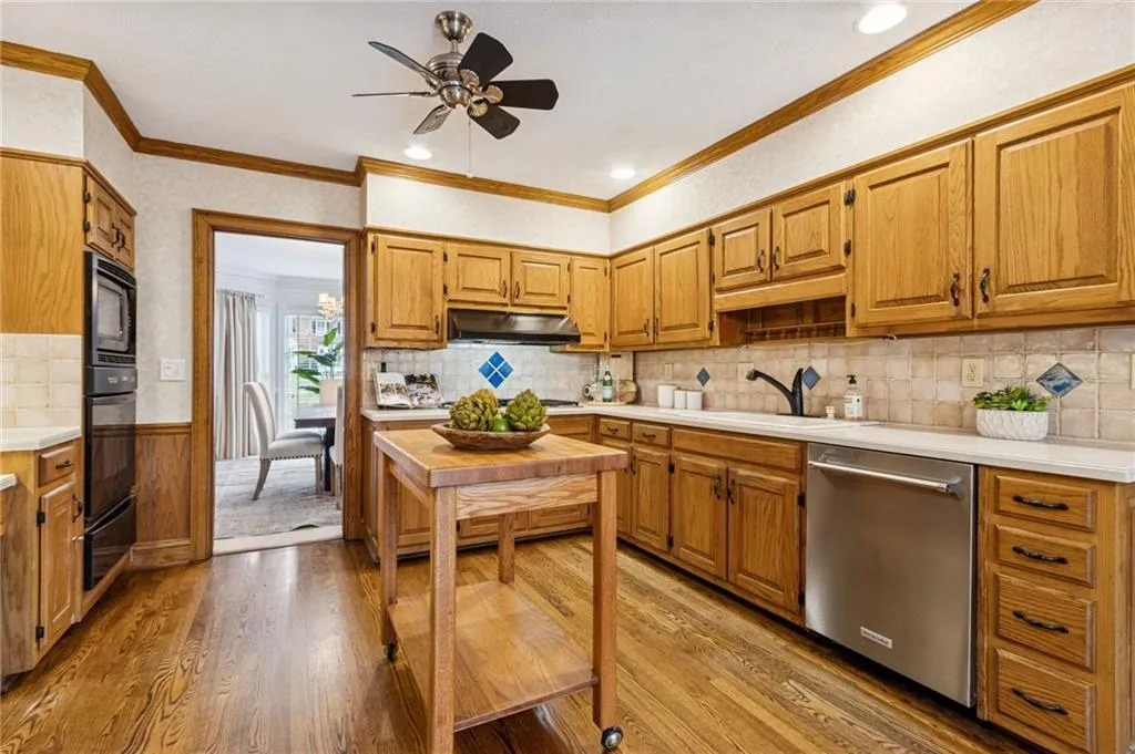 Kitchen featuring light countertops, wood finish cabinets, a ceiling fan, light wood finished floors, and a wainscoted wall