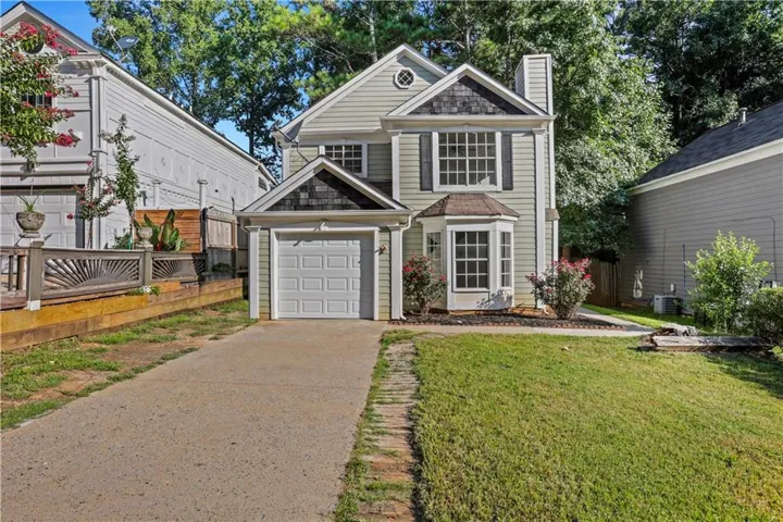Two-story colonial with gray vinyl siding and white trim features a front-gable roofline, paired windows with white frames, and an attached single-car garage with white paneled doors
