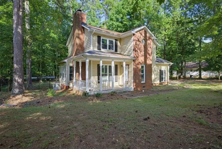 Two-story residence with a brick chimney, light-toned siding, and a covered porch