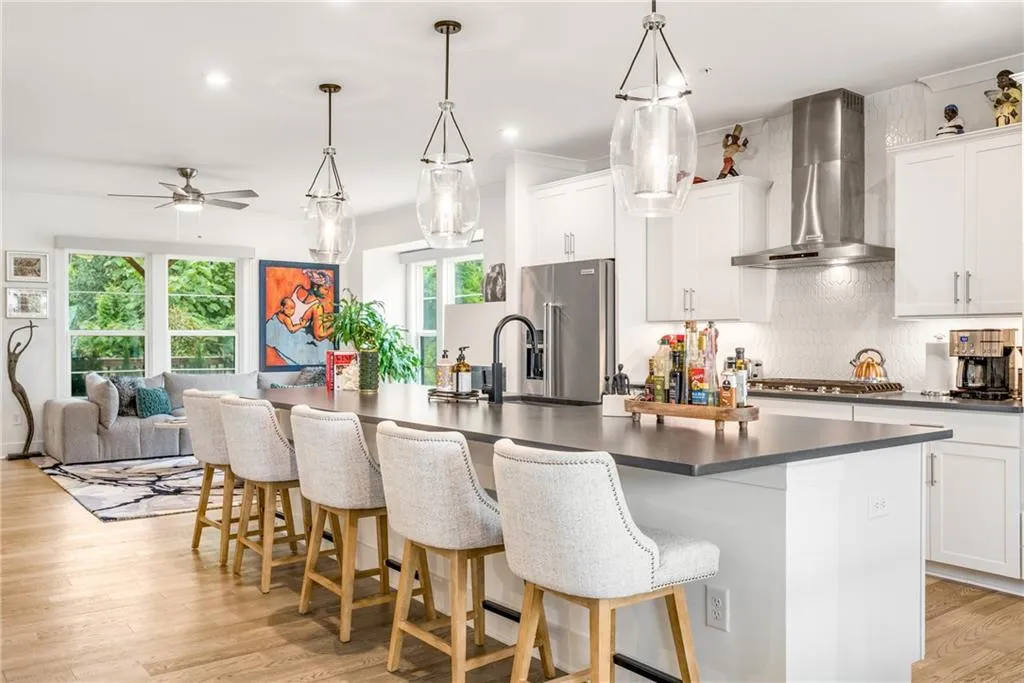 Kitchen featuring light wood-style flooring, dark countertops, wall chimney exhaust hood, tasteful backsplash, and a center island with sink