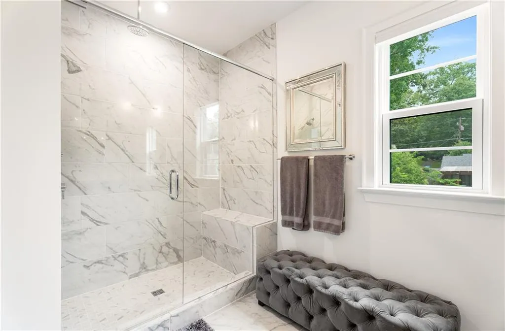 Bathroom featuring a marble finish shower, healthy amount of natural light, and marble look tiles
