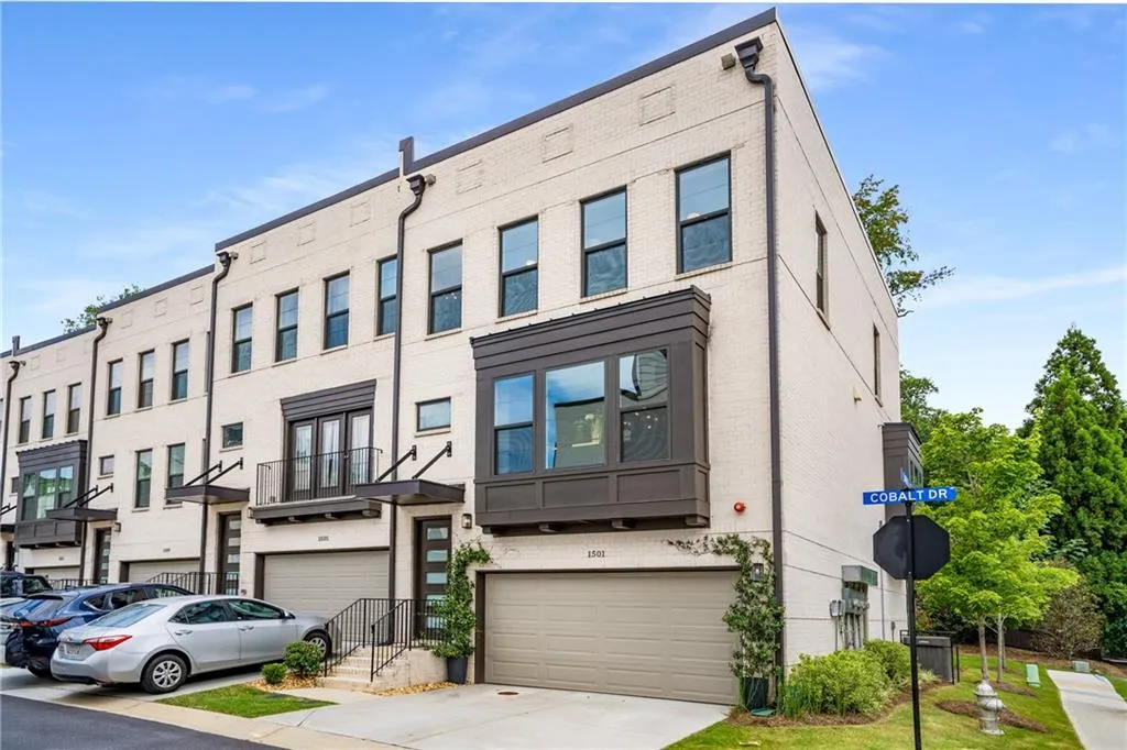 View of front of property featuring brick siding, an attached garage, concrete driveway, and a balcony