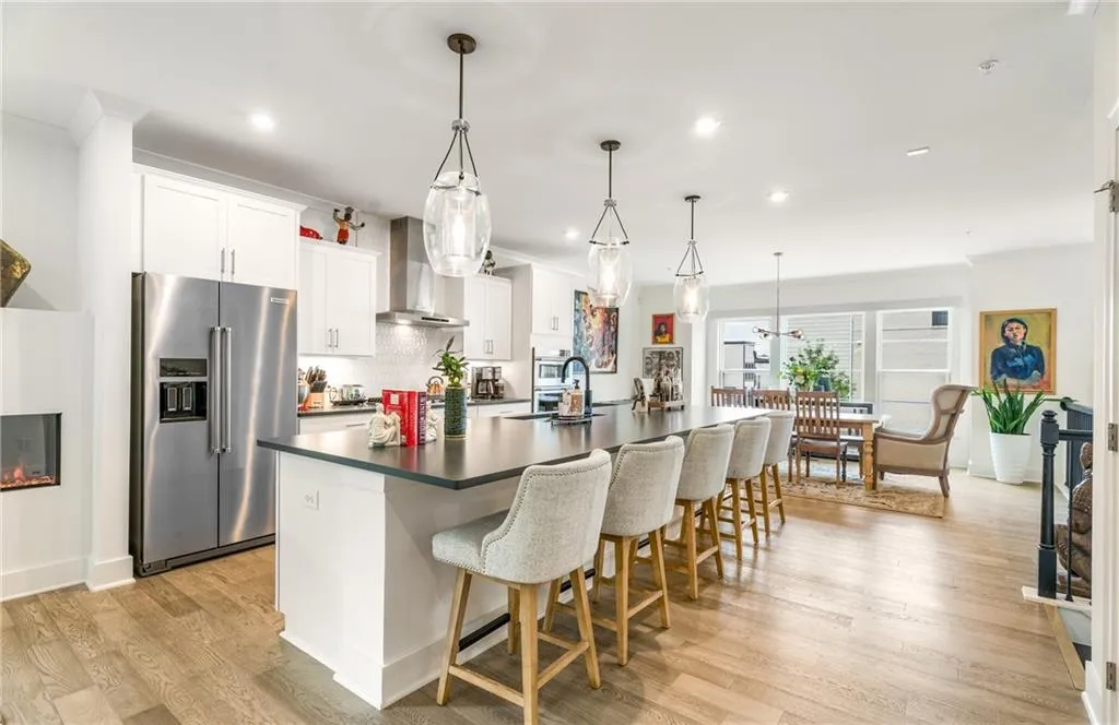 Kitchen with stainless steel appliances, a large island with sink, dark countertops, backsplash, and wall chimney range hood