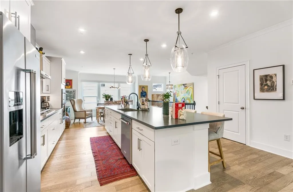 Kitchen with stainless steel appliances, dark countertops, a kitchen island with sink, white cabinets, and a breakfast bar