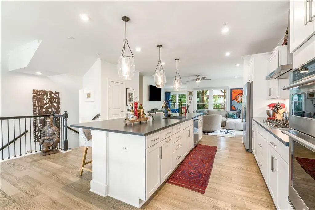 Kitchen with open floor plan, dark countertops, light wood finished floors, a center island with sink, and white cabinetry