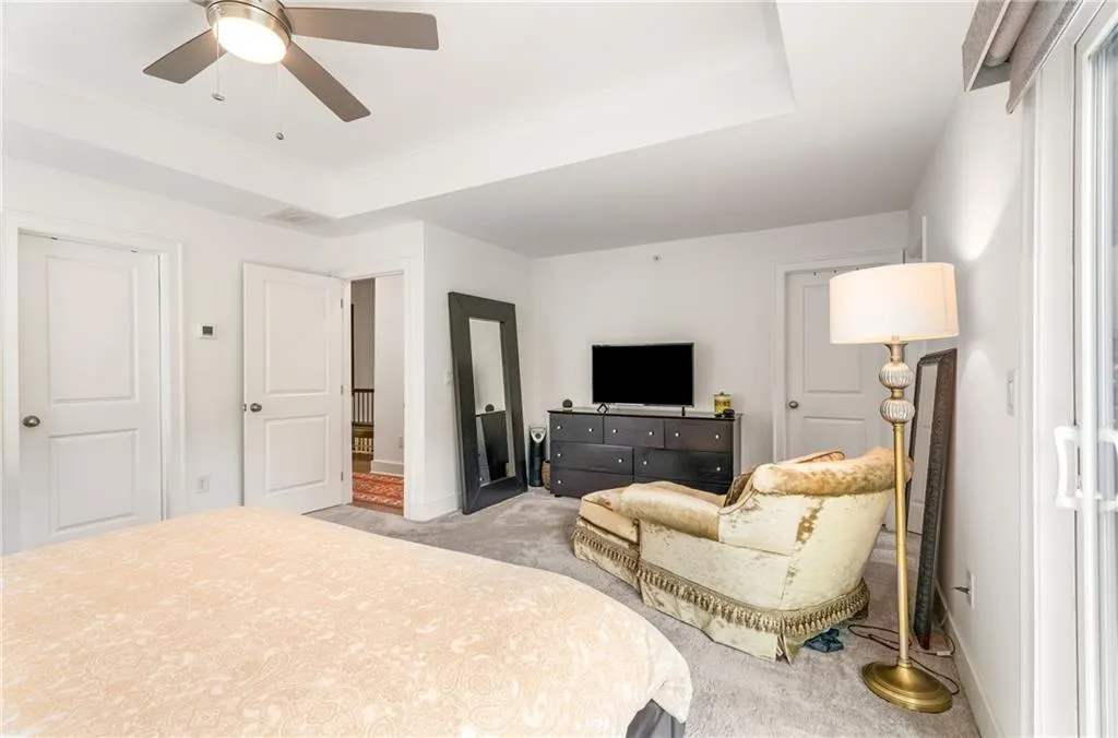 Bedroom with light carpet, ceiling fan, and a raised ceiling