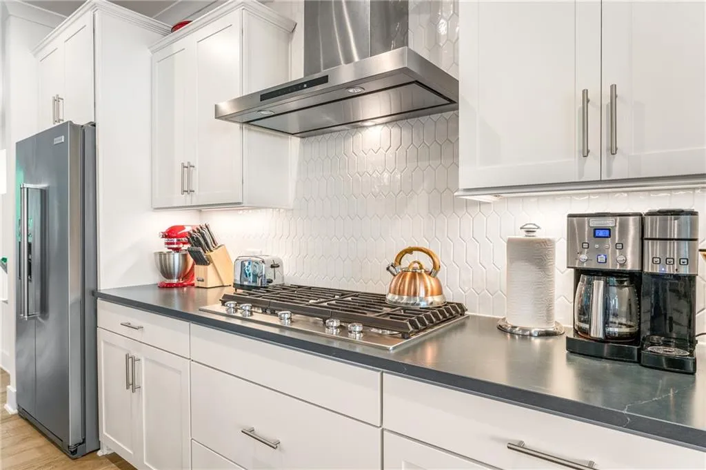 Kitchen with wall chimney range hood, backsplash, appliances with stainless steel finishes, dark countertops, and white cabinets