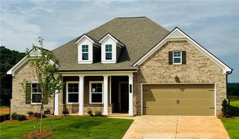Traditional-style residence featuring a brick facade with a prominent front porch supported by white columns, a two-car garage, and dormer windows accenting the roofline