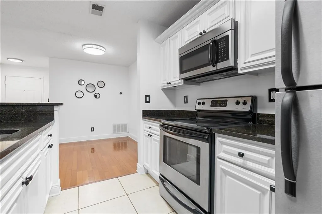 Kitchen with light tile patterned floors, visible vents, white cabinets, appliances with stainless steel finishes, and dark stone countertops