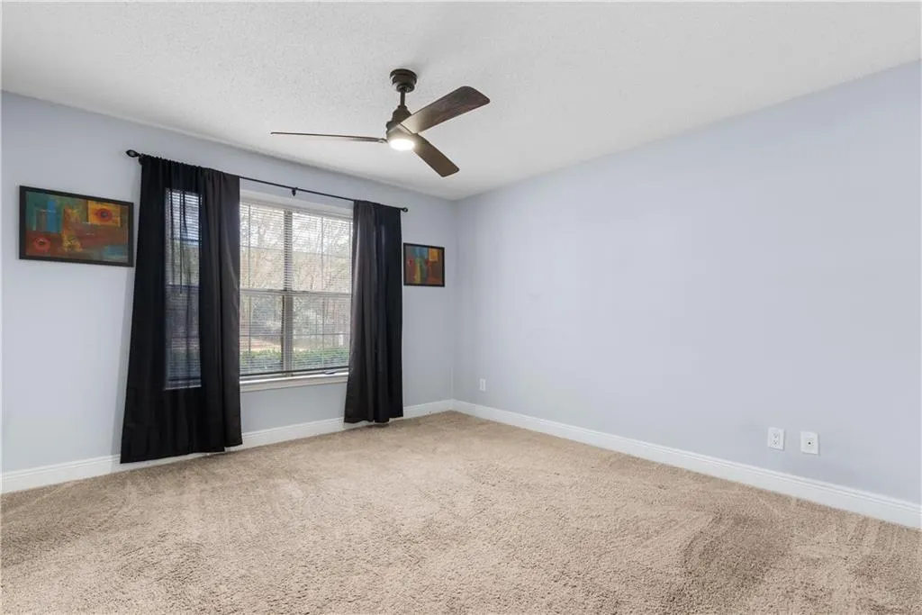 Carpeted spare room with ceiling fan, baseboards, and a textured ceiling