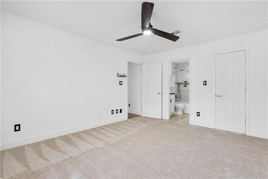 Unfurnished bedroom featuring light carpet, visible vents, baseboards, a ceiling fan, and ensuite bath