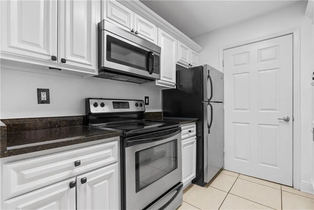 Kitchen featuring stainless steel appliances, white cabinets, dark stone countertops, and light tile patterned floors