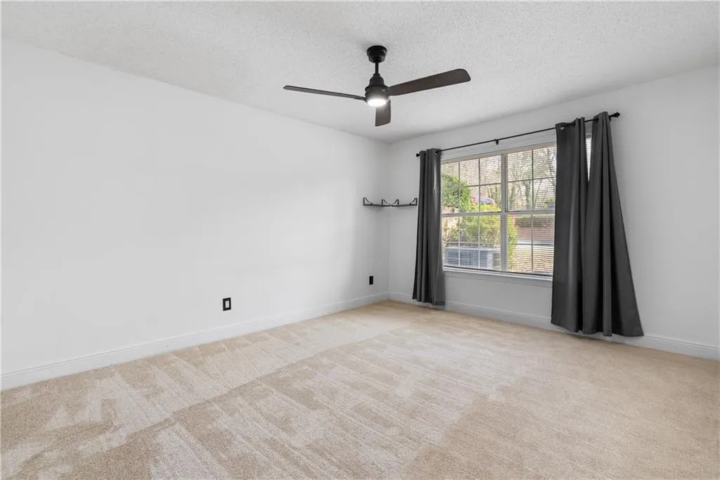 Empty room featuring a ceiling fan, light colored carpet, a textured ceiling, and baseboards