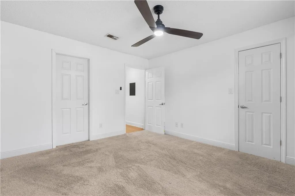 Unfurnished bedroom with light colored carpet, a ceiling fan, baseboards, visible vents, and electric panel