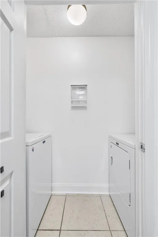 Washroom featuring laundry area, light tile patterned flooring, a textured ceiling, and washing machine and clothes dryer