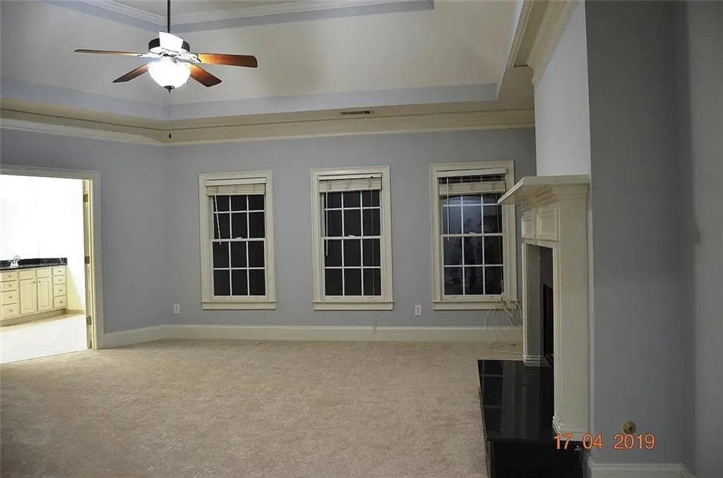 Unfurnished living room with a tray ceiling, light colored carpet, a ceiling fan, and a fireplace