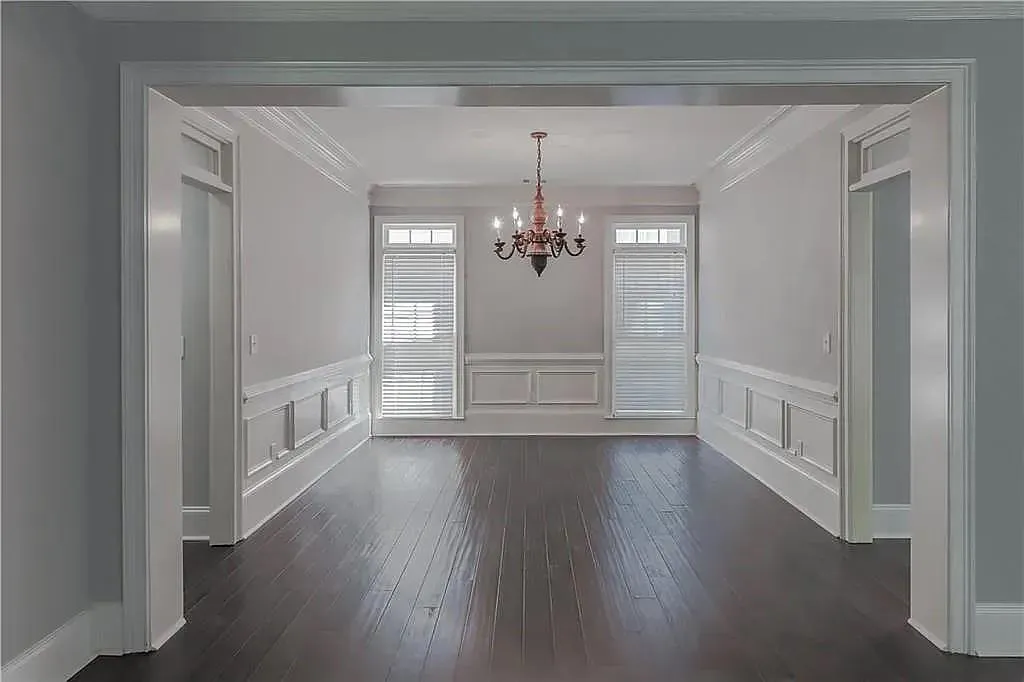 Unfurnished dining area featuring ornamental molding, a chandelier, a decorative wall, a wainscoted wall, and dark wood-style flooring