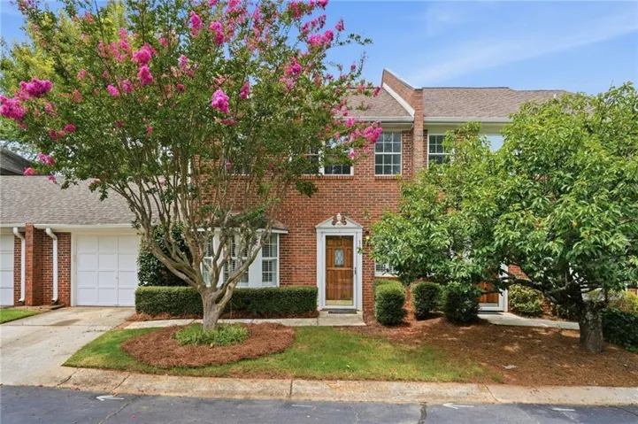 Brick townhouse exterior with multiple windows, featuring a prominent flowering tree and an attached garage