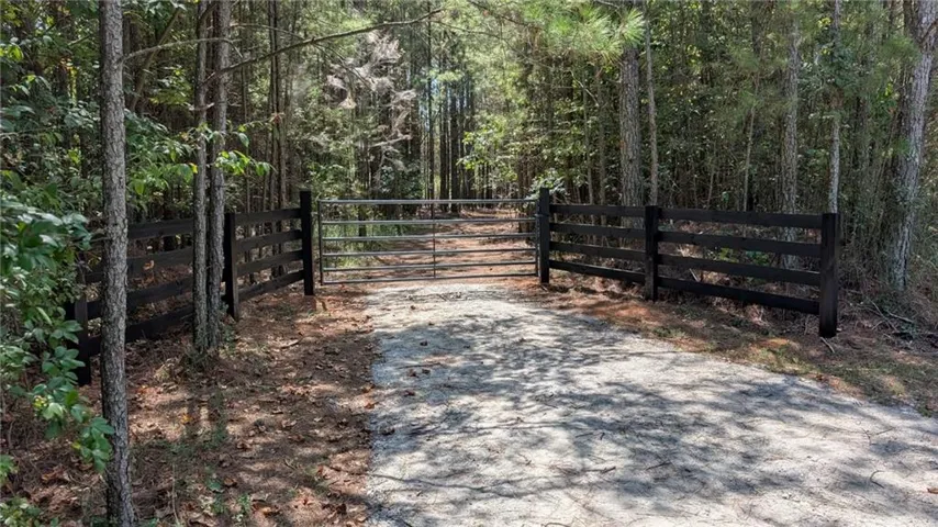 Gated entry with a gravel drive, surrounded by mature trees and a dark wood-finish fence