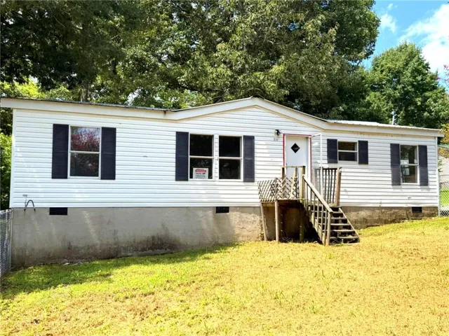 White vinyl siding exterior with dark shutters, front porch with wooden steps, and chain-link fencing