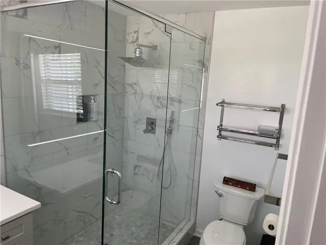 Modern bathroom featuring a glass-enclosed shower with a rainfall showerhead, marble-look tile surround, and pebbled floor