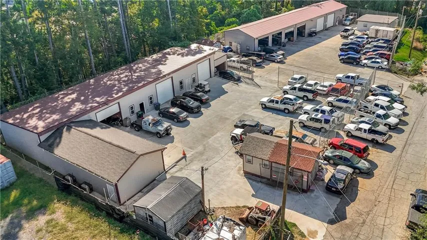 Multiple commercial buildings, expansive paved lot, security fencing, and mature trees along the property perimeter