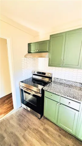 Kitchen featuring light green cabinetry, a stainless steel range, and a white geometric tile backsplash