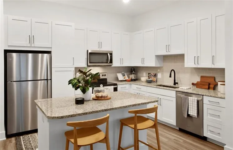 Kitchen featuring stainless steel appliances, a breakfast bar, light stone counters, and white cabinets