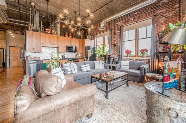 Exposed brick walls, wood-finish flooring, high ceilings with exposed ductwork, modern industrial lighting, and a kitchen featuring wood cabinetry and stainless steel appliances