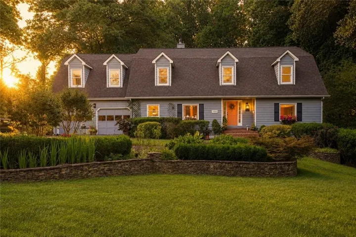 Dormer-style residence featuring light blue siding with dark shutters, a front entry with an orange door, and an attached garage