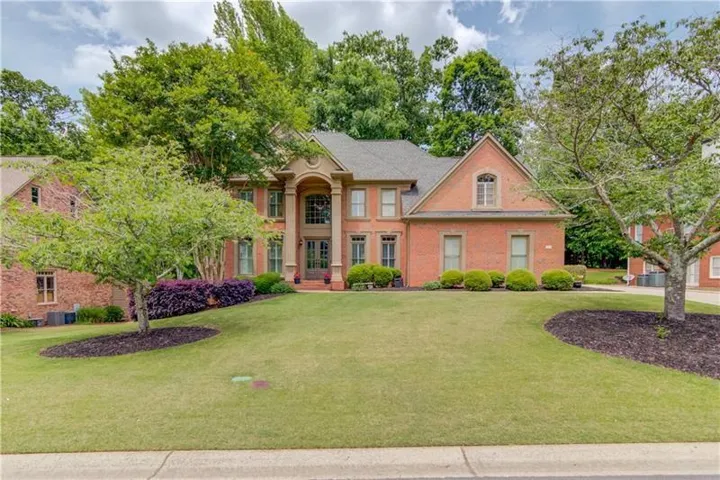 Brick exterior with a grand two-story entry, mature trees, manicured lawn, and established landscaping