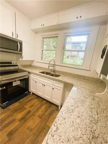 Kitchen featuring appliances with stainless steel finishes, white cabinetry, light stone countertops, and dark wood-style flooring