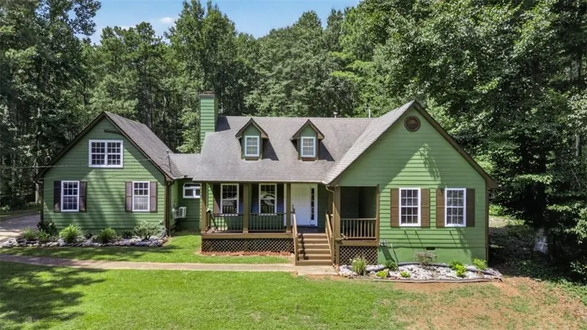 Green siding exterior with white window frames and dark shutters, featuring a covered front porch, dormer windows, and a prominent chimney
