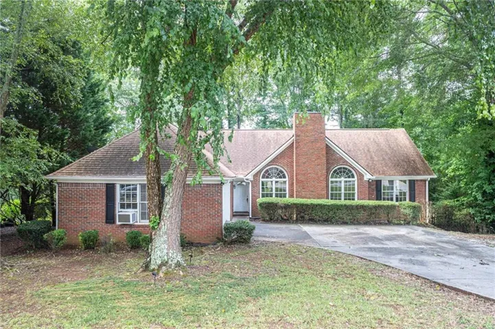 Brick exterior with a prominent chimney, arched windows, gabled roofline, and a paved driveway