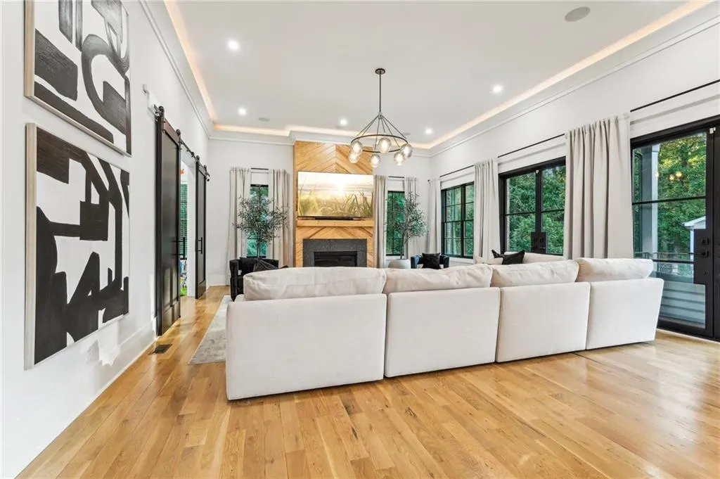 Living room with a large fireplace, light hardwood / wood-style flooring, a chandelier, a barn door, and crown molding