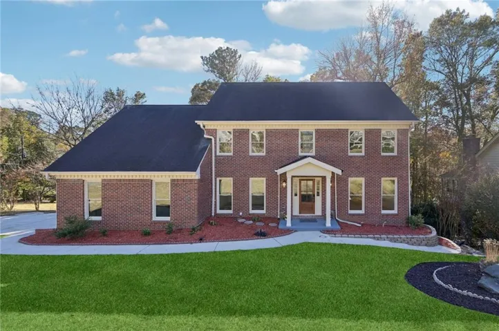 Brick exterior featuring multiple windows, dark shingle roof, and a covered entry