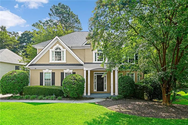 Two-story stucco residence featuring a prominent front gable with an arched window, a covered porch with white columns, and dark shutters