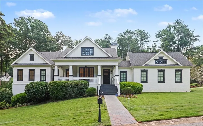 White exterior with dark trim windows, covered porch, brick walkway, and sloped lawn
