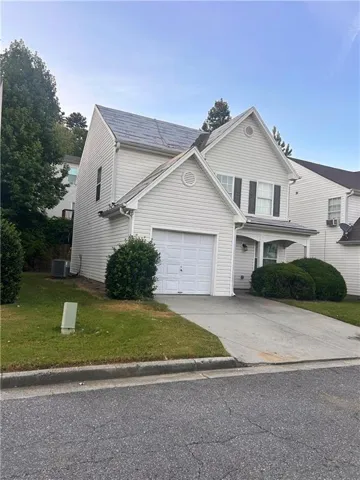 Exterior featuring light-colored siding, an attached garage, a paved driveway, and established landscaping
