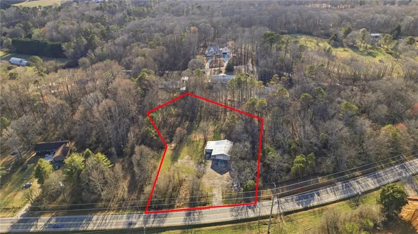 Aerial view of property and surrounding area with property parcel outlined and a forest