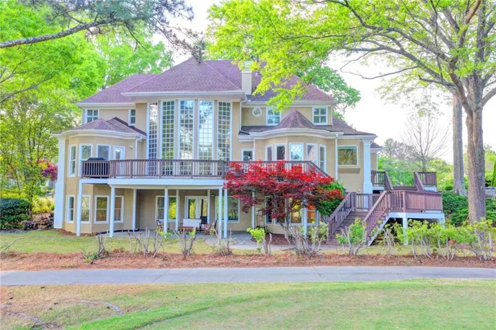 Stucco exterior featuring extensive fenestration, a full-width upper-level deck, a lower-level patio, and multi-level outdoor access