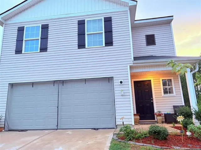 Light-toned siding exterior featuring a covered entry, dark paneled front door, and a two-car garage