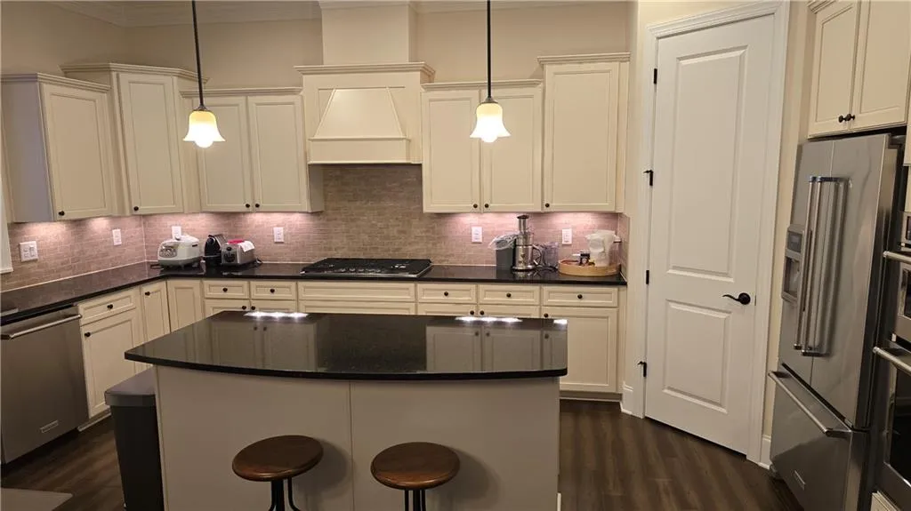 Kitchen with dark countertops, premium range hood, appliances with stainless steel finishes, and dark wood-type flooring