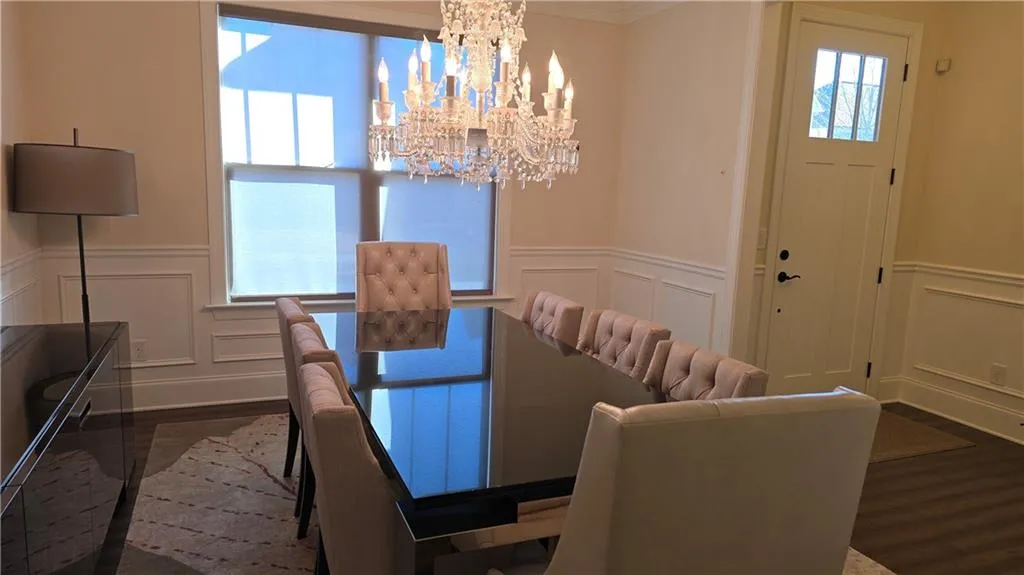 Dining space with a wainscoted wall, a decorative wall, dark wood-style flooring, and a chandelier